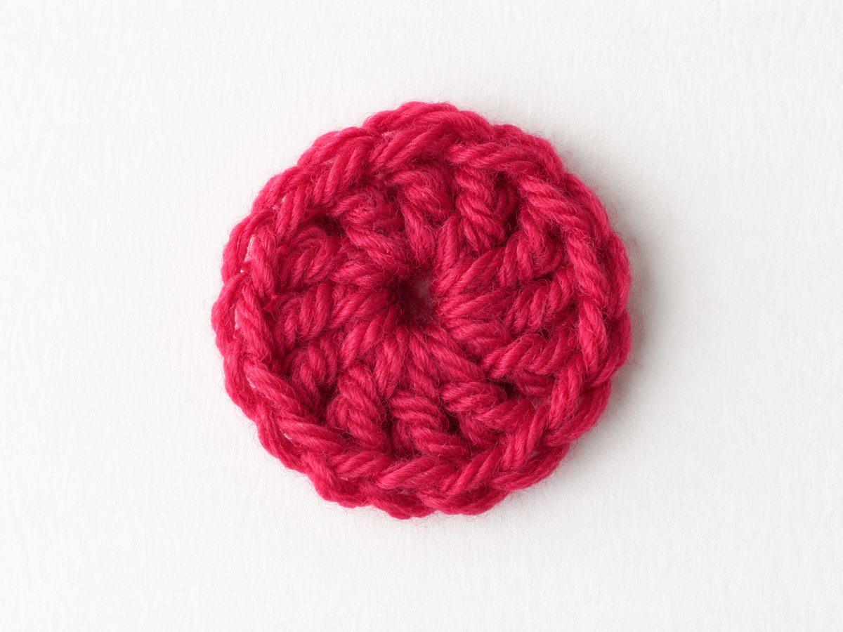 Round 1 wheel of the flower worked in deep raspberry yarn, ten spokes around a small center hole