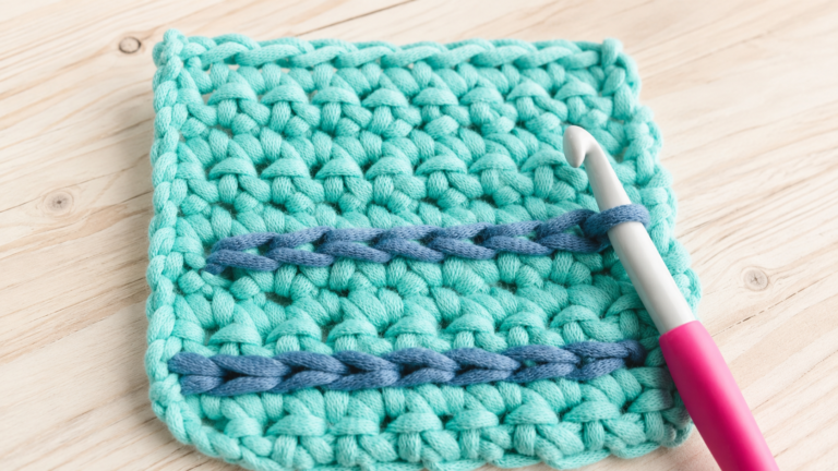 Close-up of a turquoise crochet swatch with a hook and contrasting blue stitches