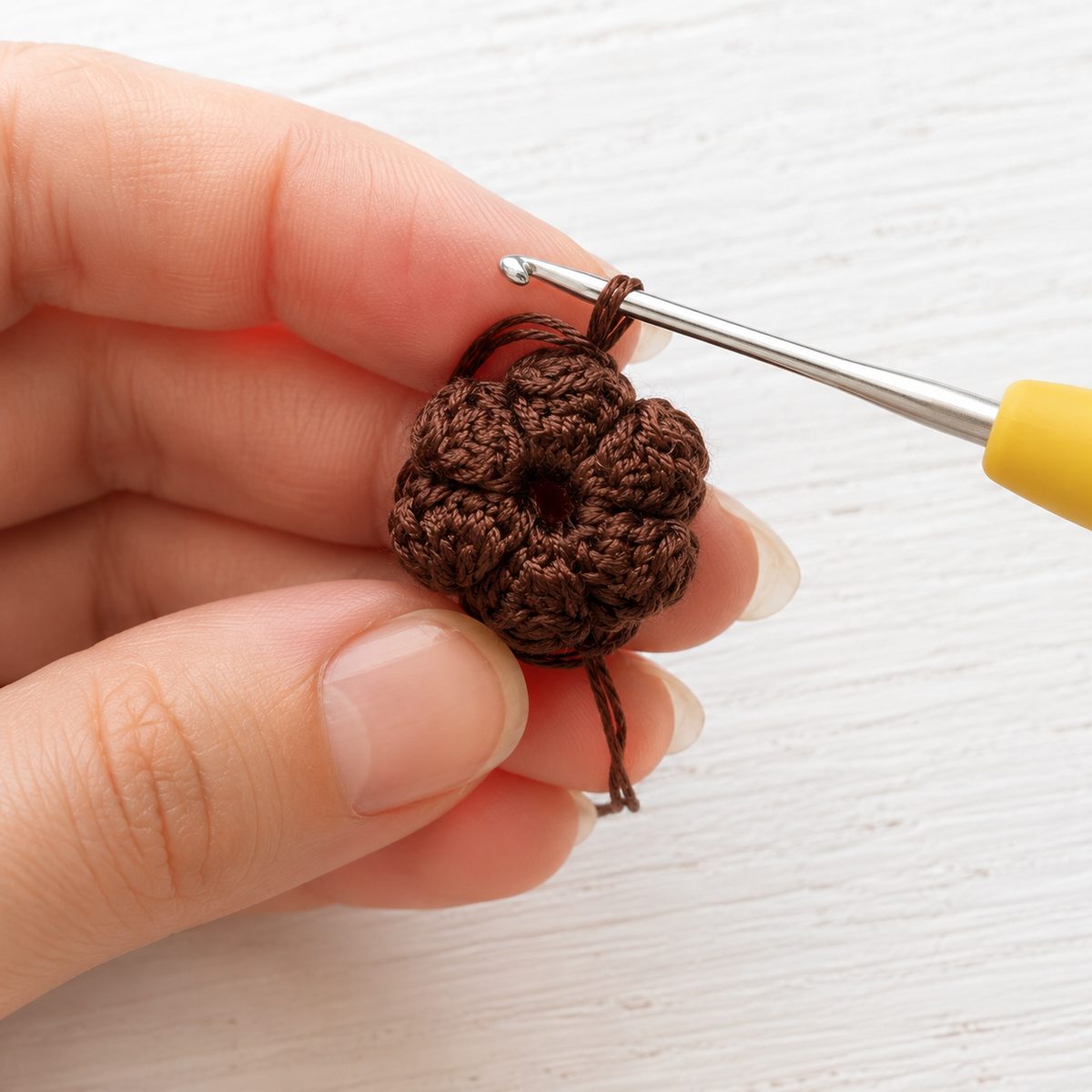 Domed brown crochet sunflower center made of popcorn stitches held between fingertips with hook