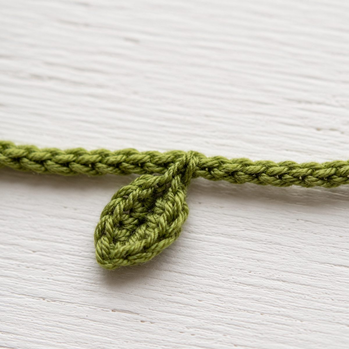 Small green crochet leaf with a center vein growing out of the vine band cord