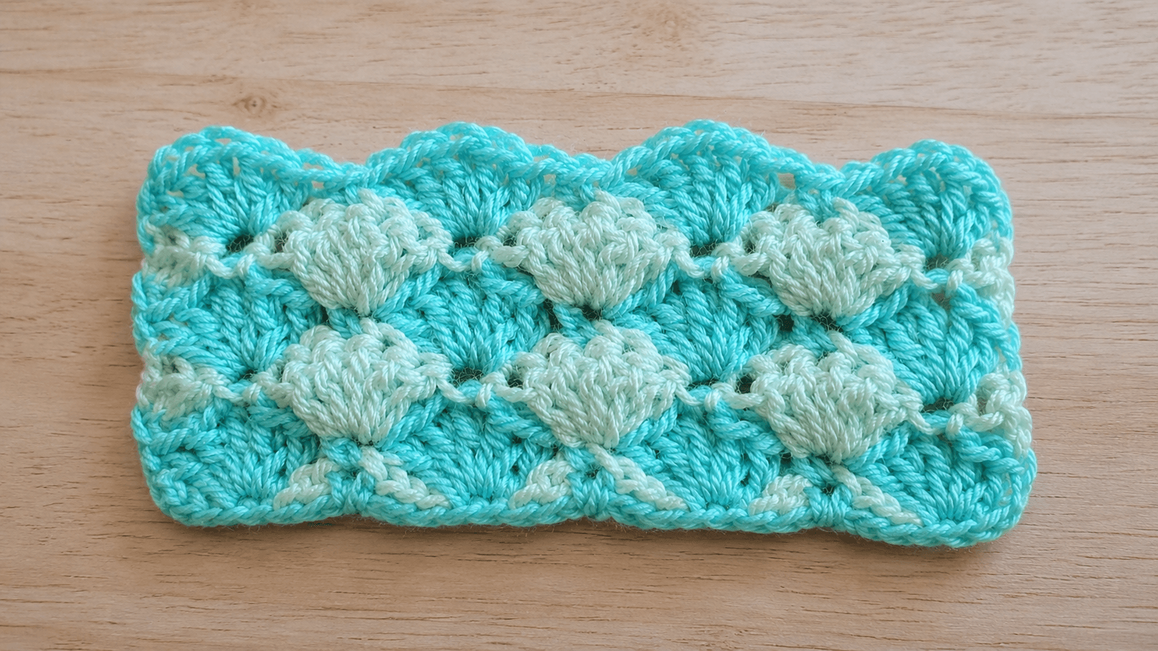 Aqua crochet swatch with raised pale green motifs and a scalloped upper edge