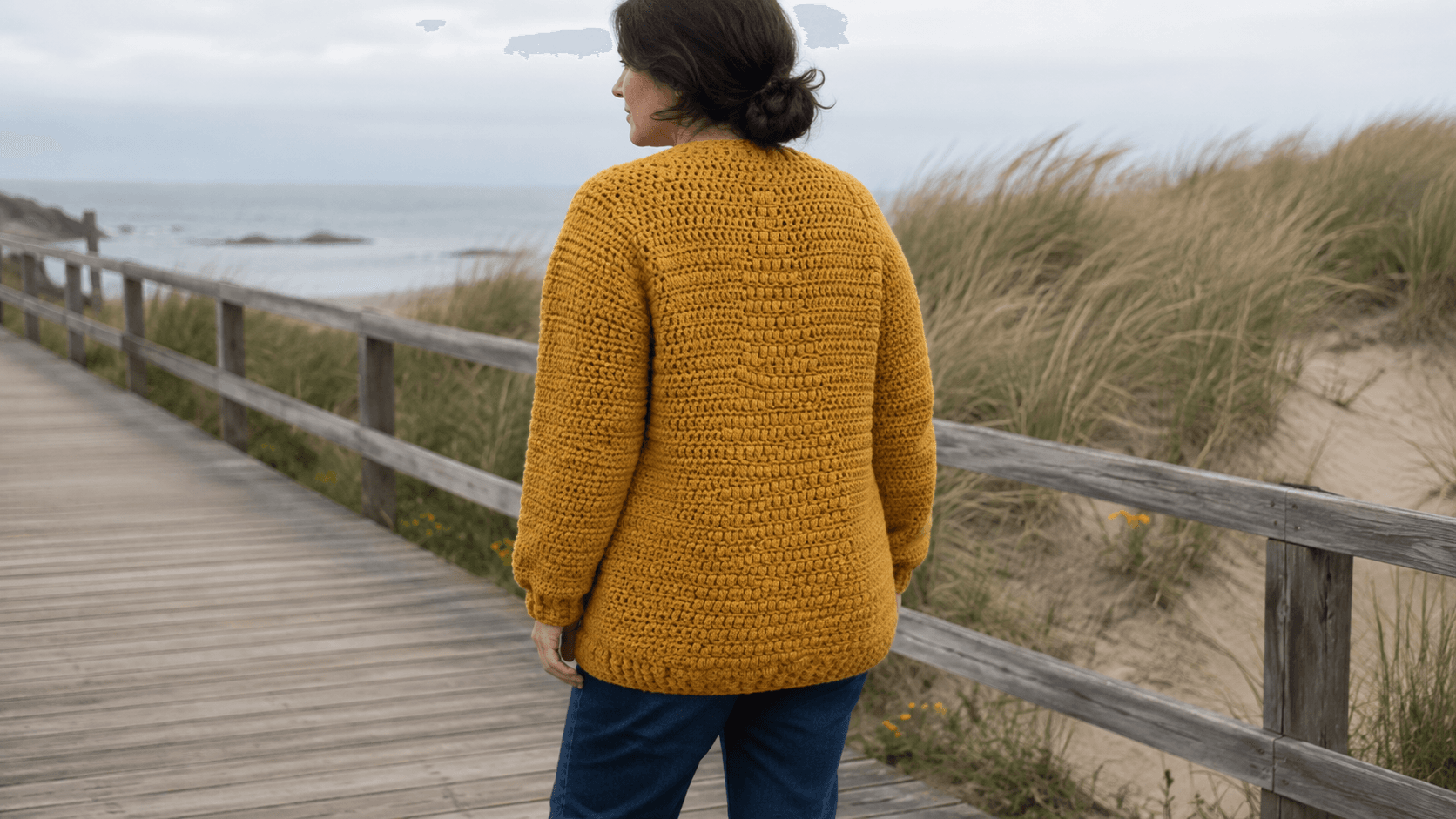 Solid mustard gold crochet puff stitch cardigan, back view, beach