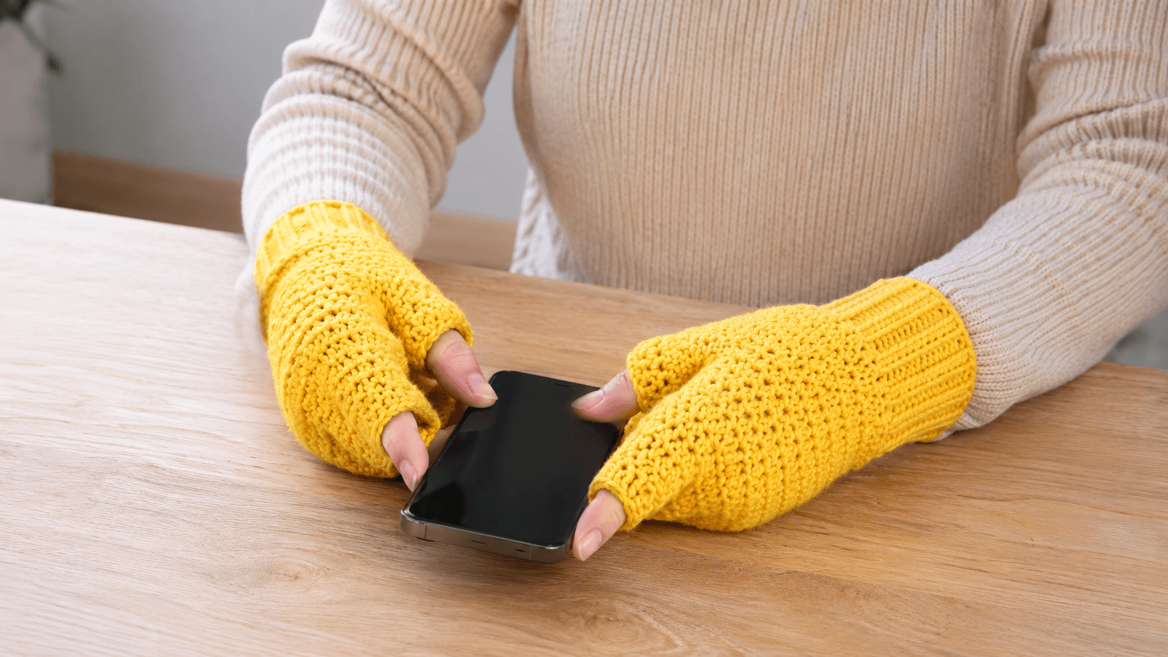 Yellow fingerless crochet mittens holding a phone