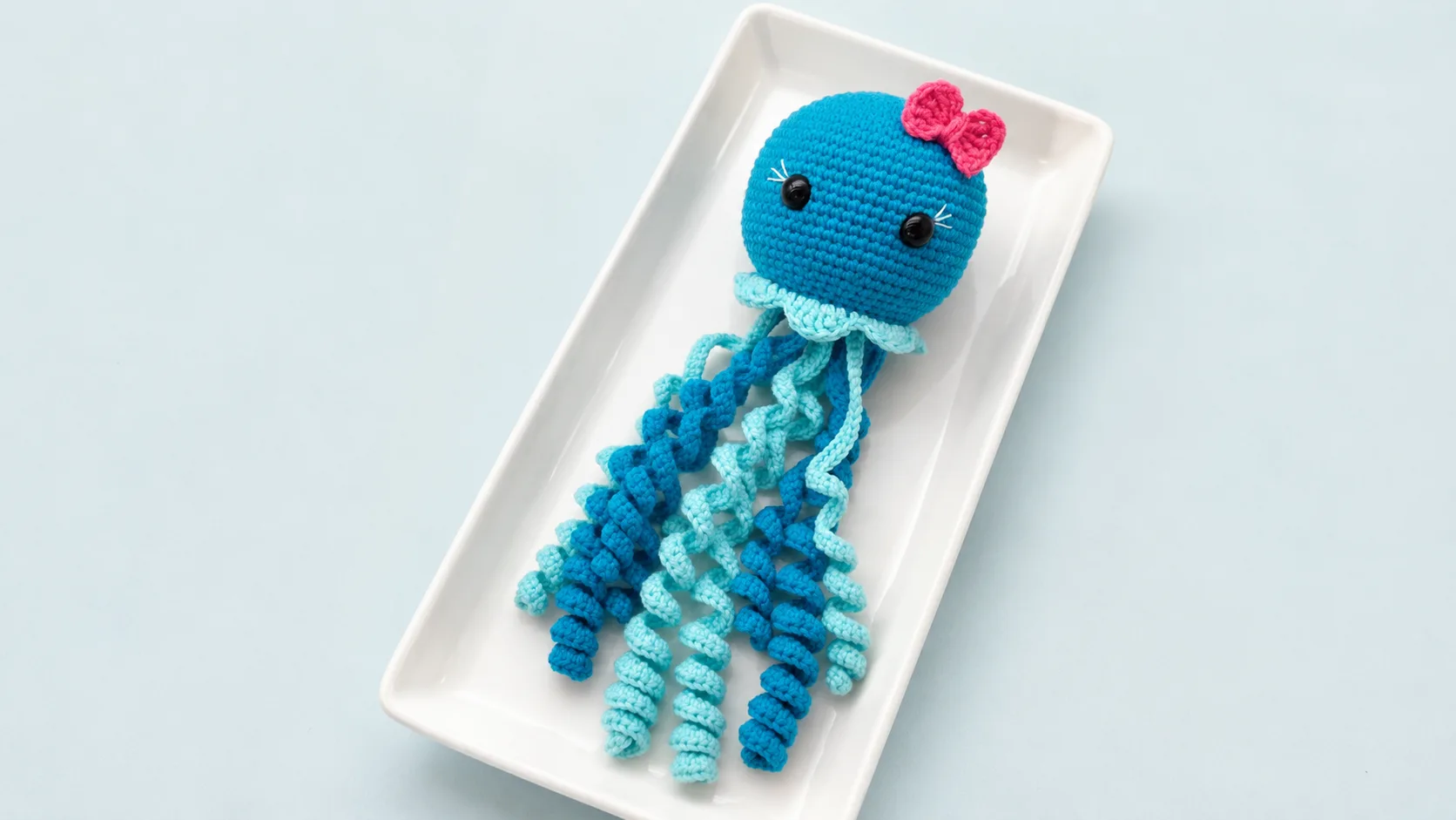 Blue crochet jellyfish with a pink bow on a white plate