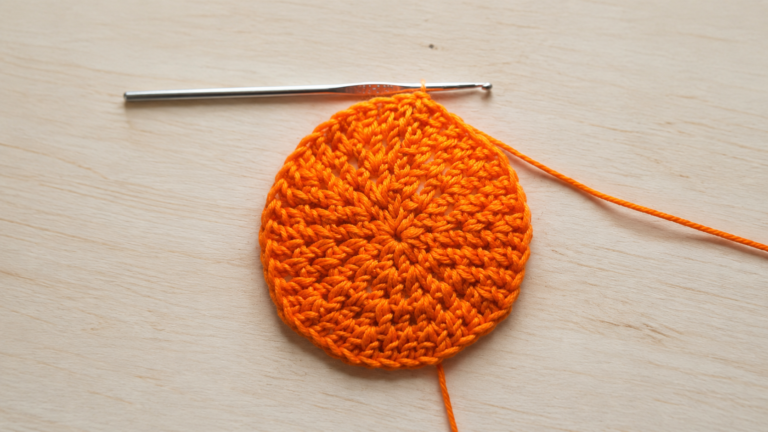 Orange flat crochet circle in progress with a crochet hook