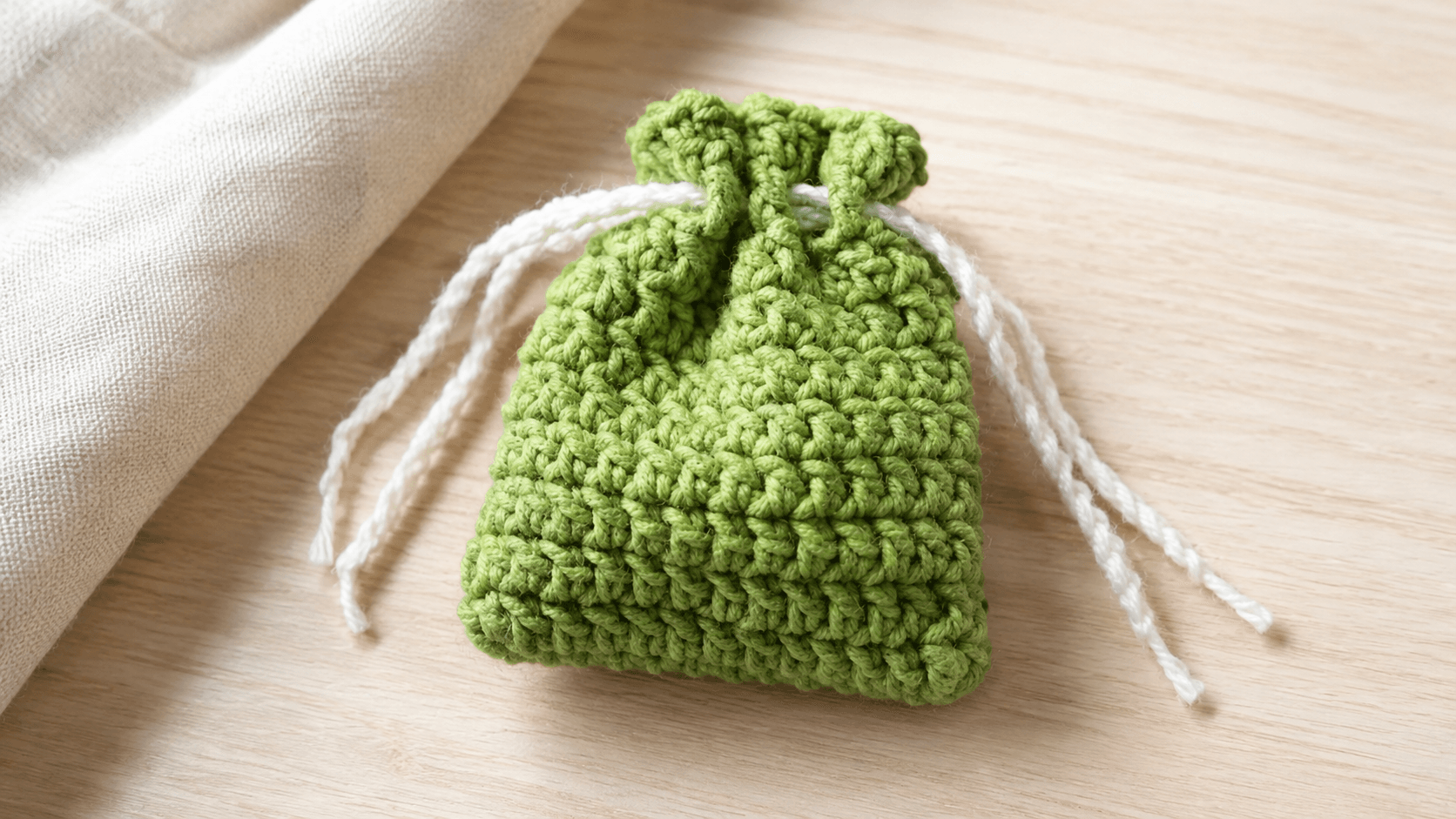 Small green crochet drawstring pouch on a wood table
