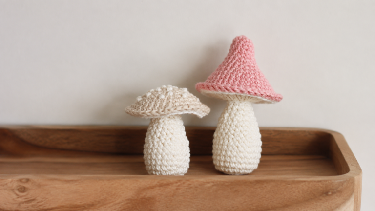 Two crocheted mushrooms with white stems and pink and cream caps