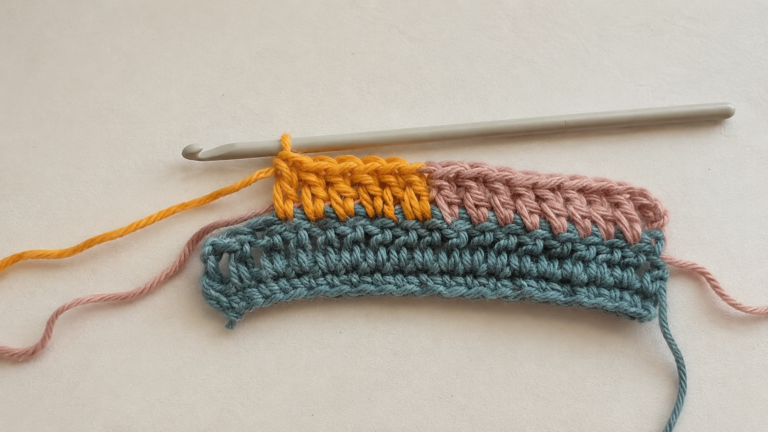 Crochet hook working a multicolor swatch with yellow, pink, and blue yarn