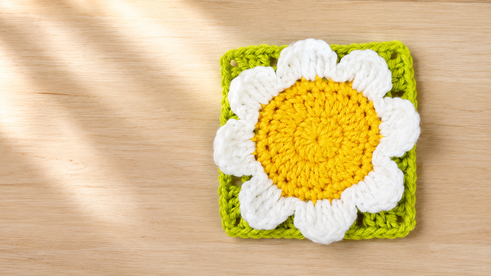 Yellow and white crochet 3D daisy granny square on a green background