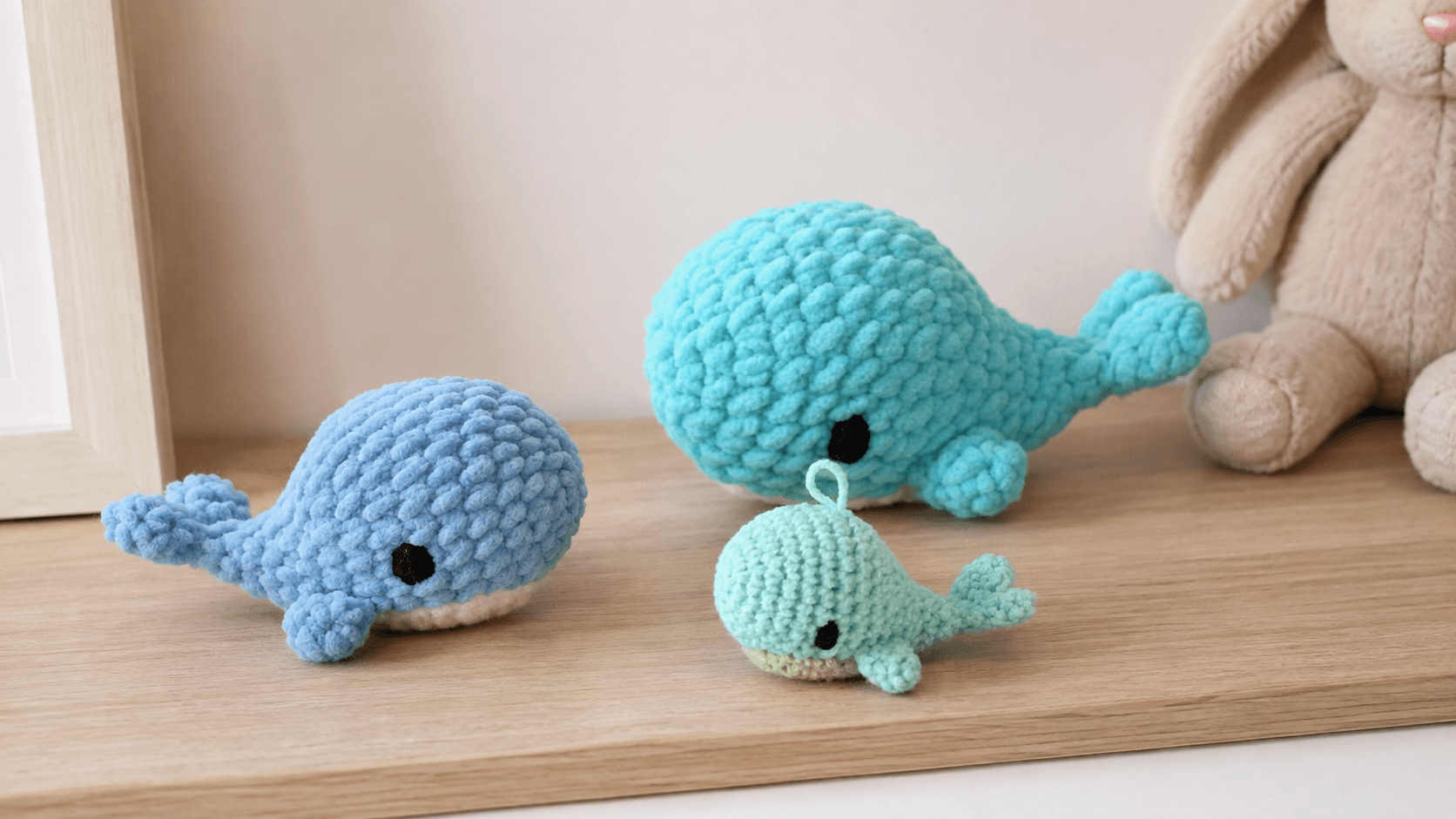 Three blue and mint crochet whale toys on a shelf