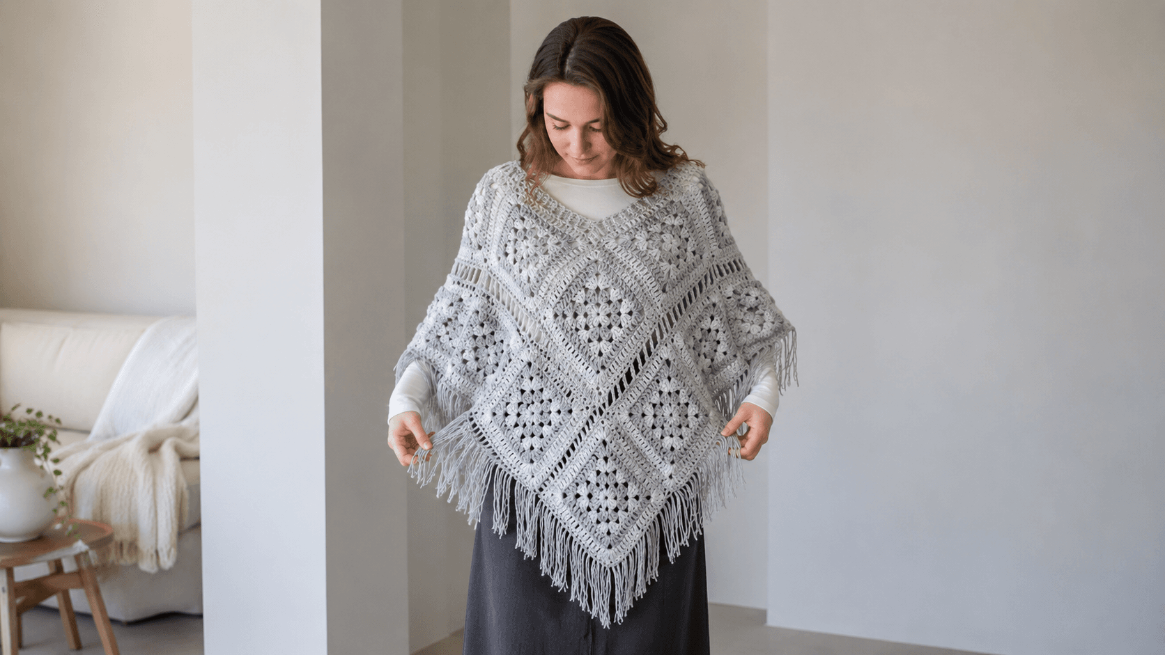 Gray and white fringed granny square crochet poncho worn by a woman