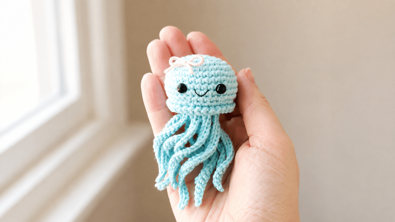 Teal crochet jellyfish with a pink bow held in a hand