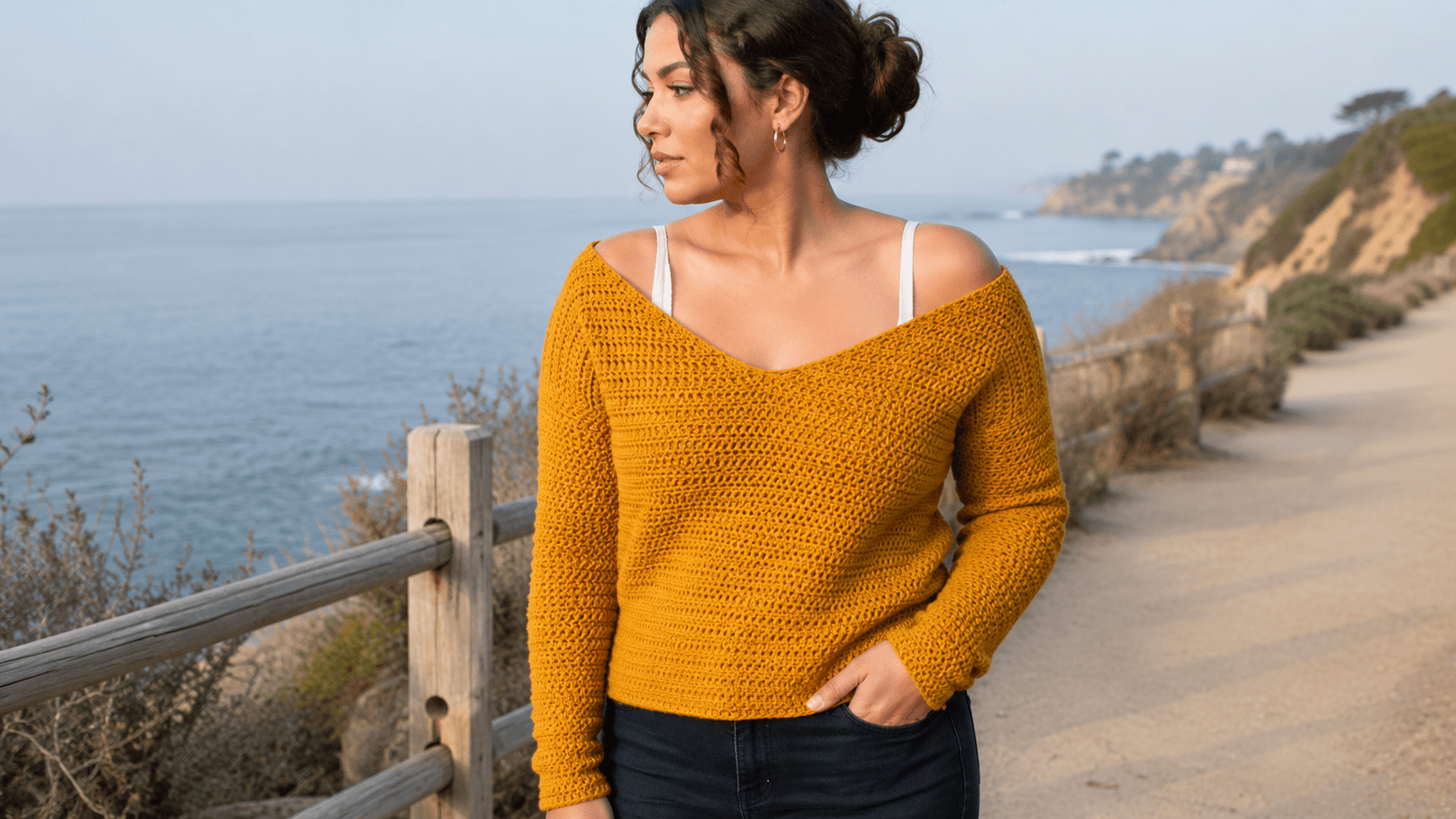 Woman wearing a mustard off shoulder crochet sweater by the ocean