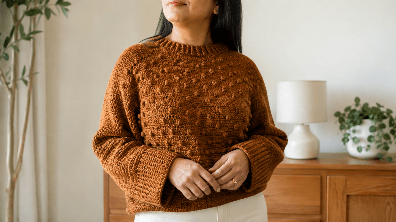 Woman wearing a rust crochet sweater with popcorn bobble texture