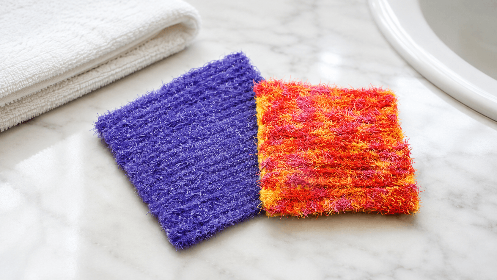 Purple and orange-red scrubby crochet dishcloths on a marble counter