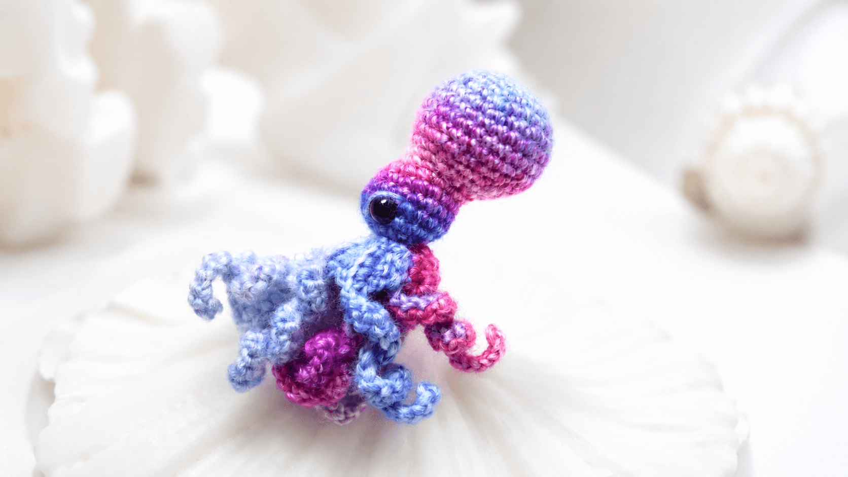 Small pink purple and blue crochet octopus, curled tentacles, white background