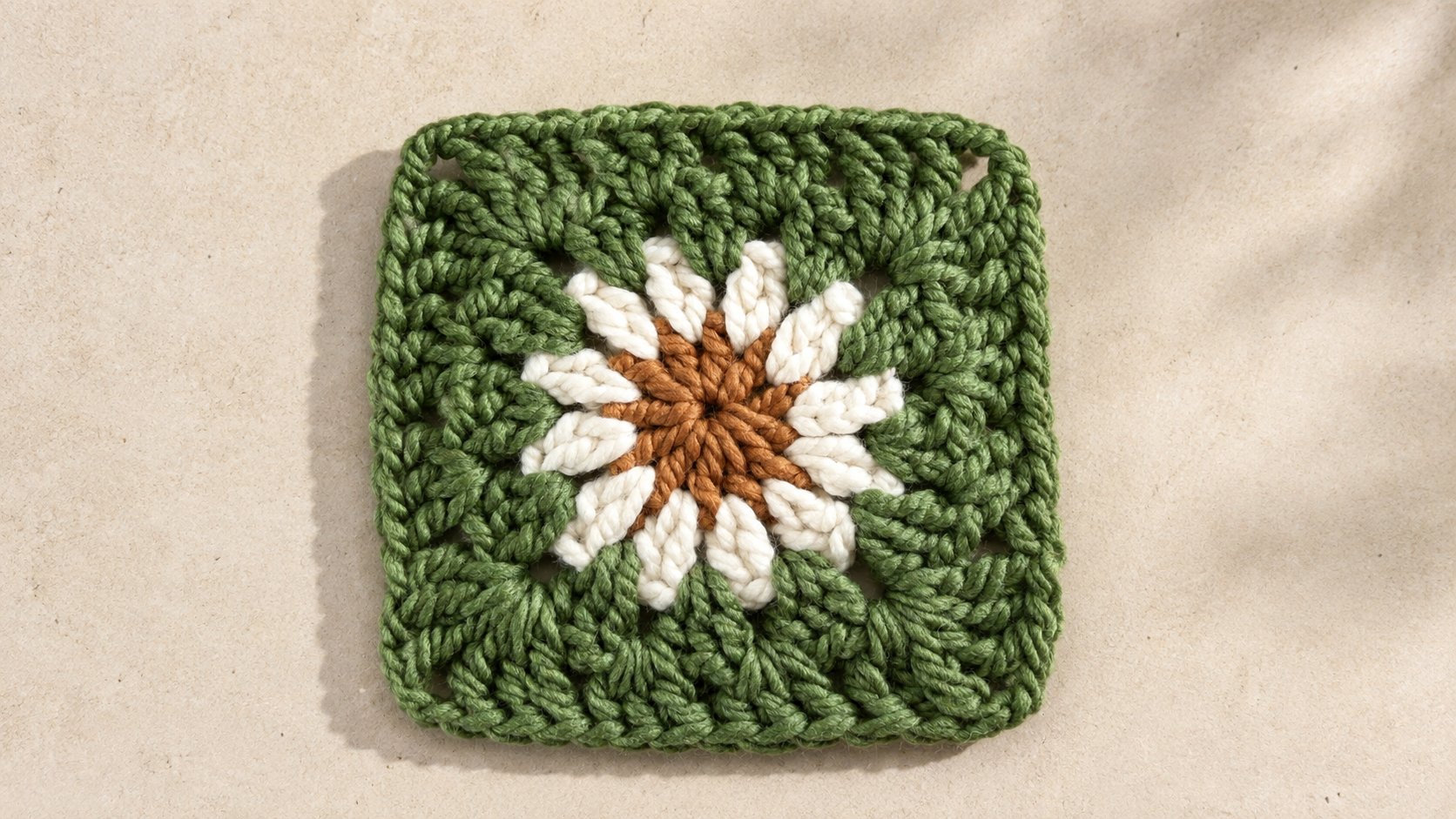 White crochet daisy granny square with an orange center on a green square