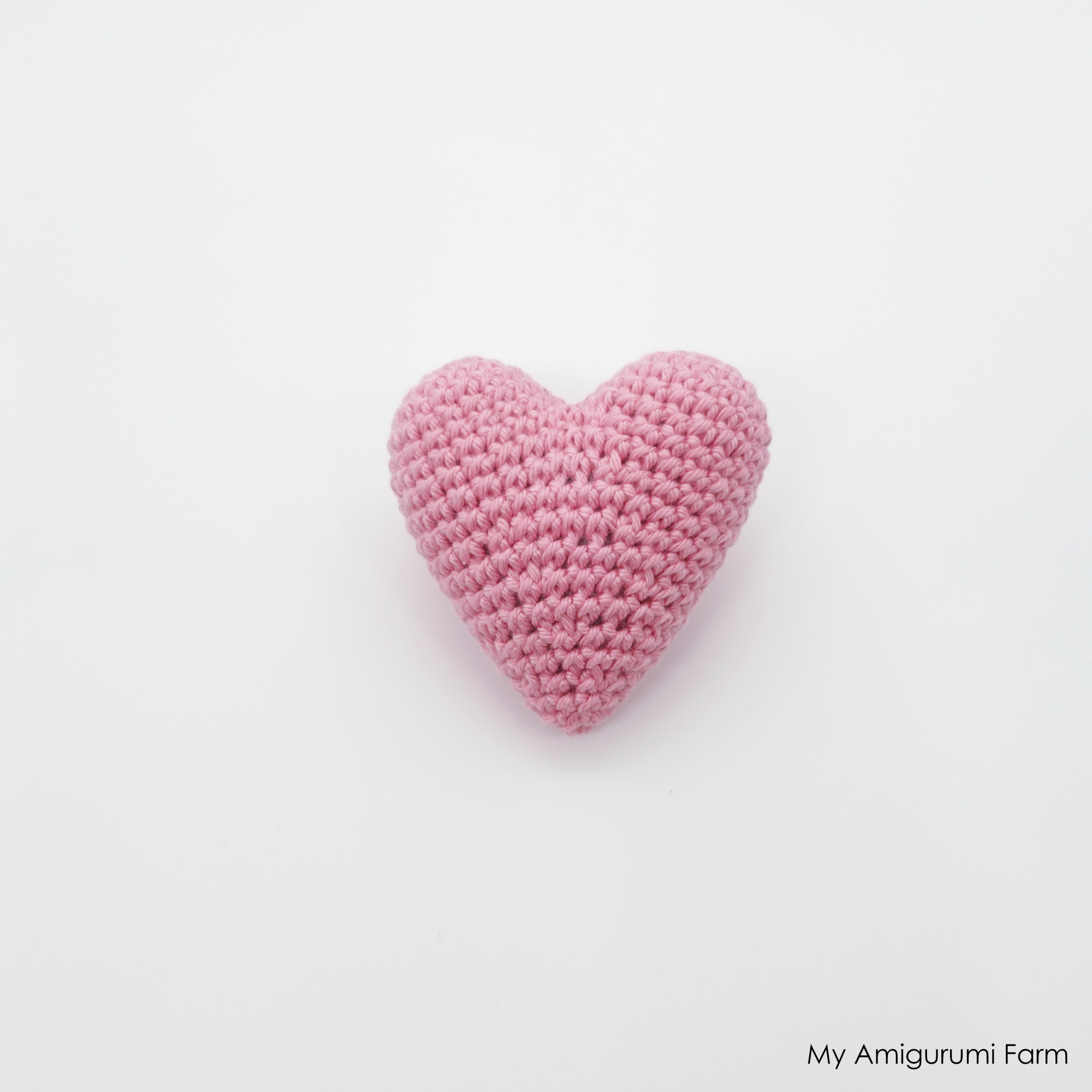 Small pink stuffed crochet amigurumi heart on a white background