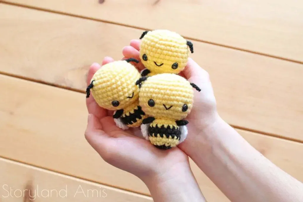 Three small yellow and black amigurumi bees held in two hands