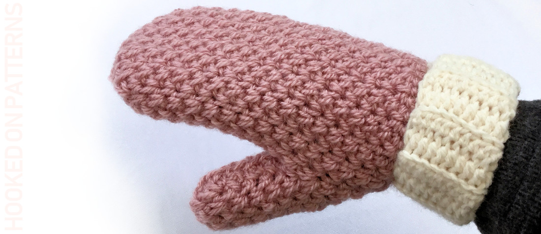 Pink crochet mitten with cream ribbed cuff worn on a hand