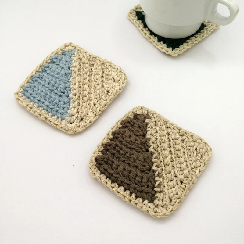 Two-tone geometric crochet coasters in blue and brown with tan trim
