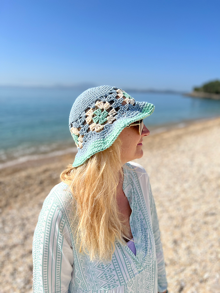Woman wearing a seafoam and cream granny square crochet bucket hat at the beach