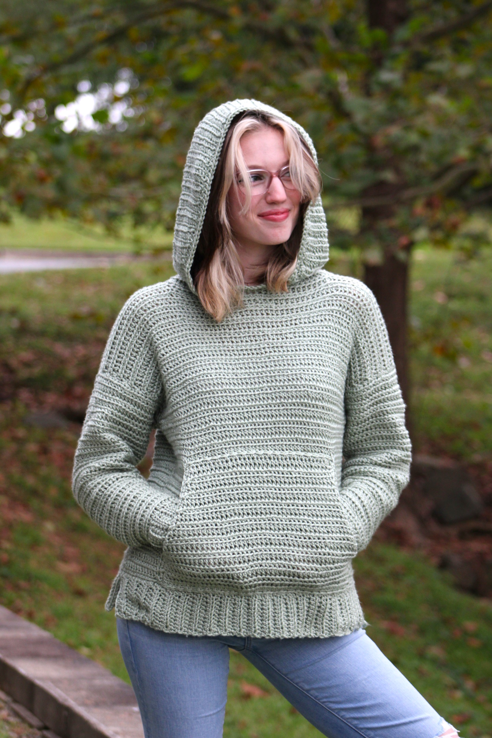 Woman wearing a sage green crochet hoodie with front pocket outdoors
