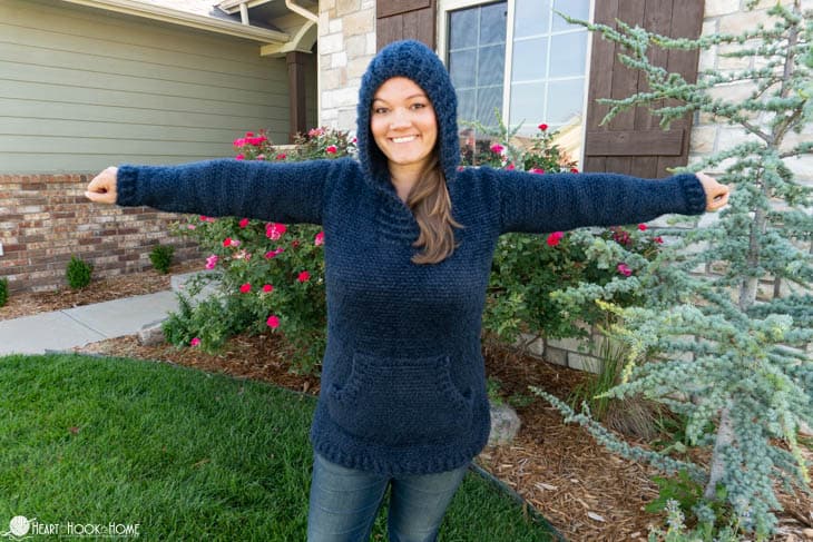 Woman wearing a navy hooded crochet sweater with front pocket outdoors