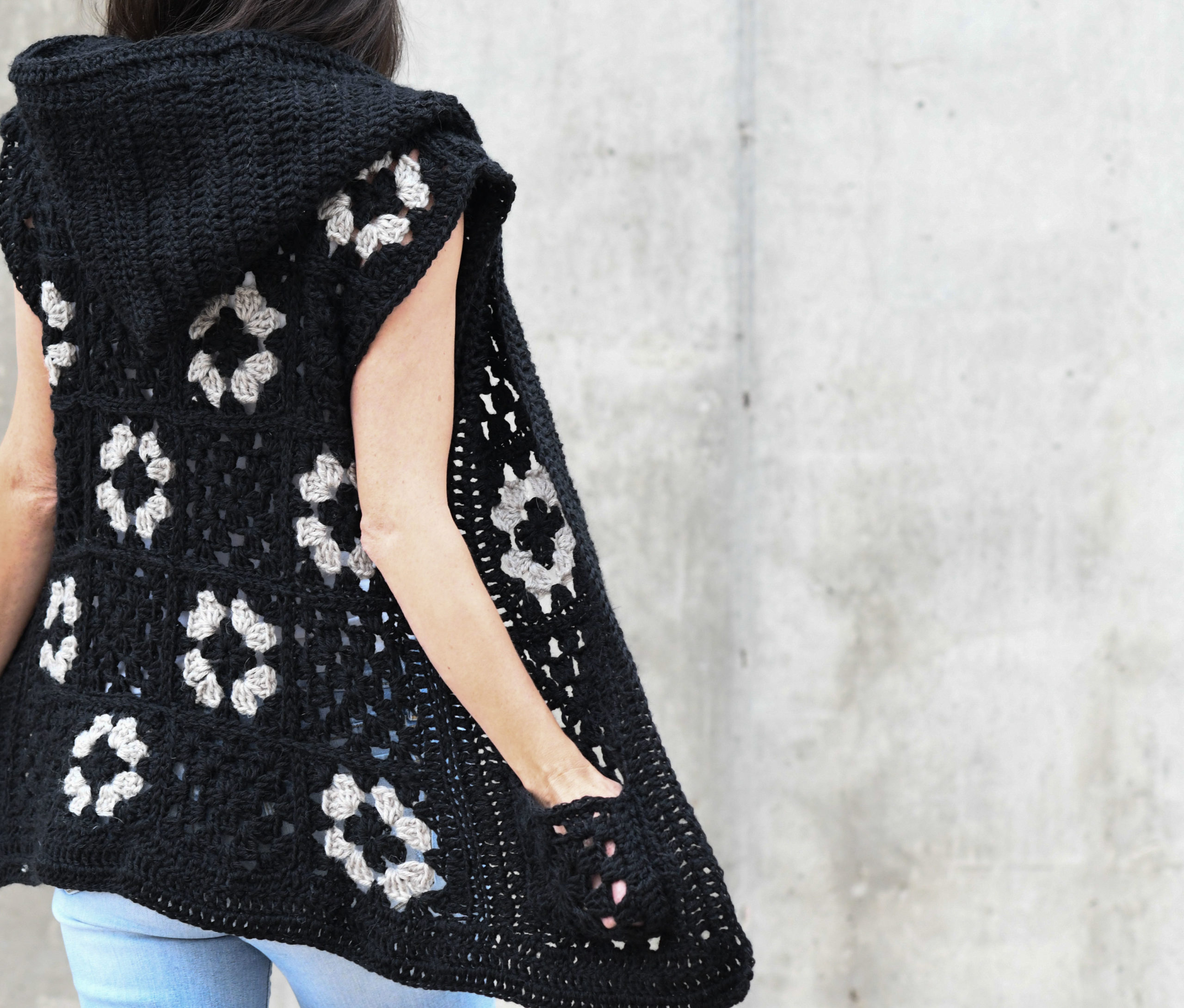 Woman wearing a black and cream hooded granny square crochet vest, back view