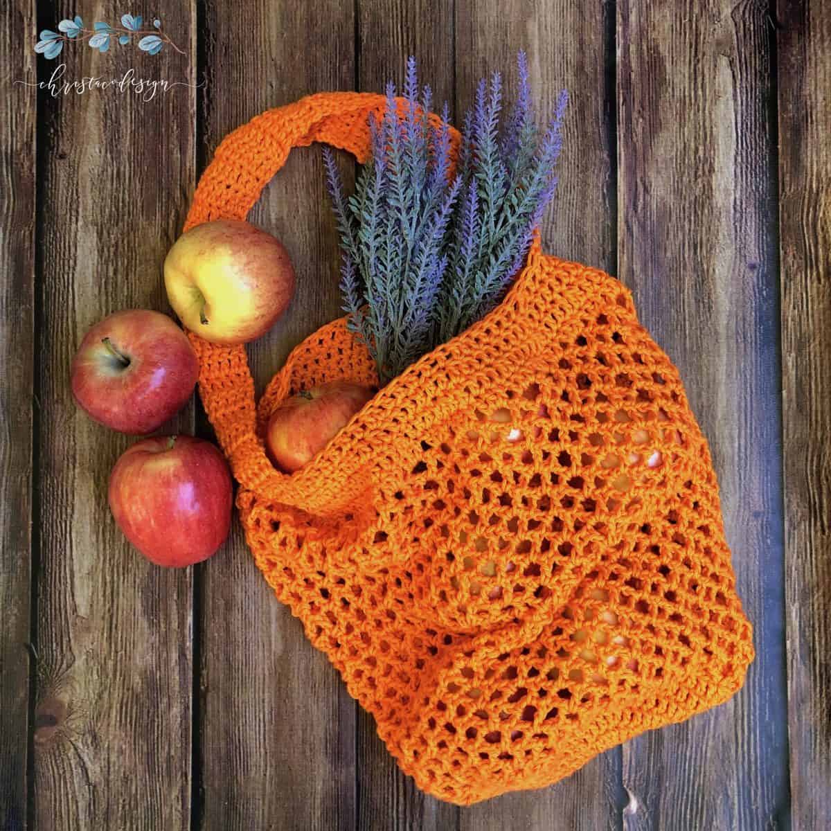Orange crochet mesh market tote bag with apples and lavender on wood background