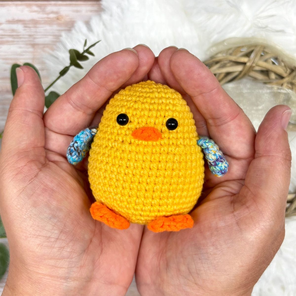 Small yellow crochet chick with blue wings held in two hands